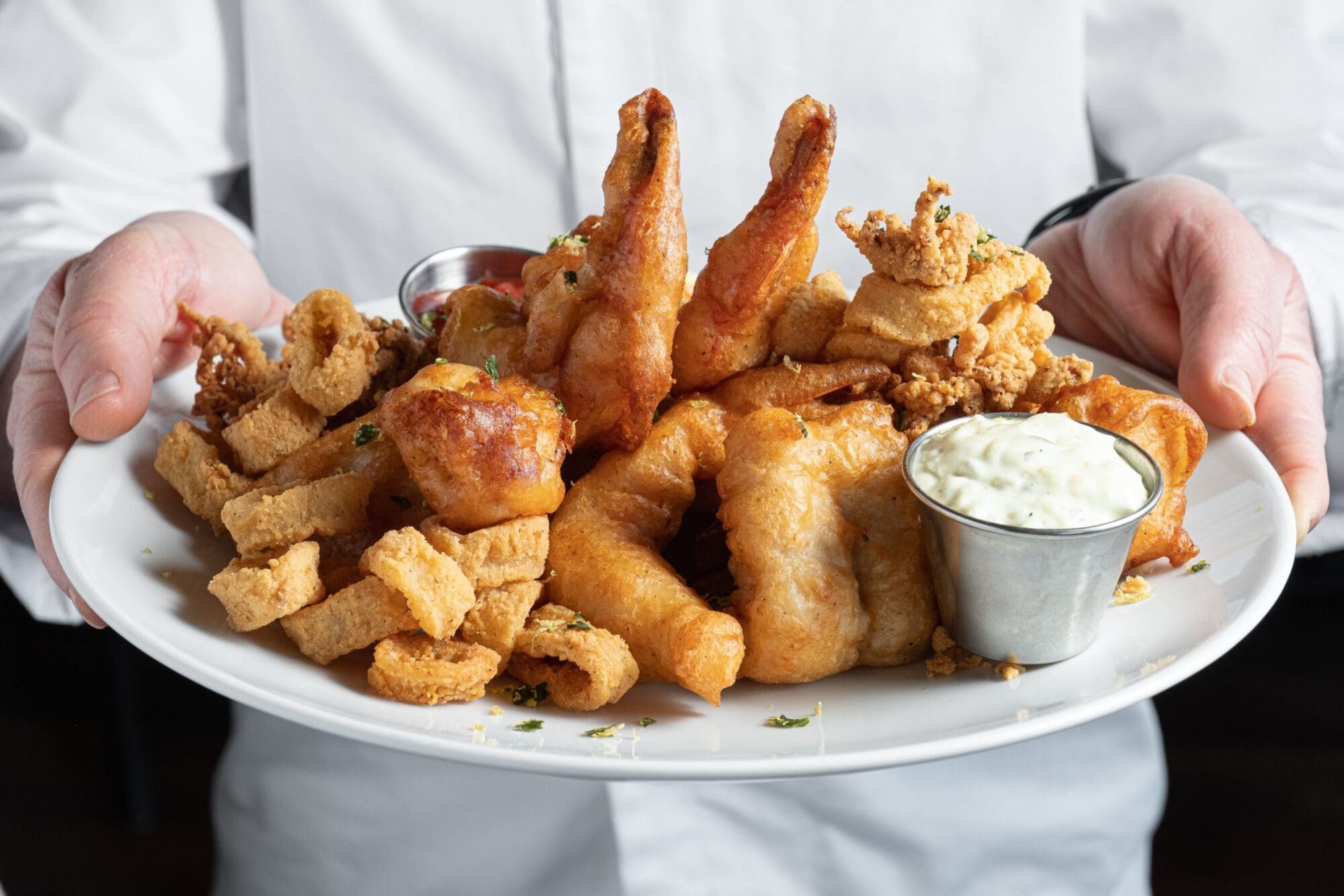 Chef holding fisherman's platter including colossal naked shrimp, sea scallops, local whitefish and calamari.