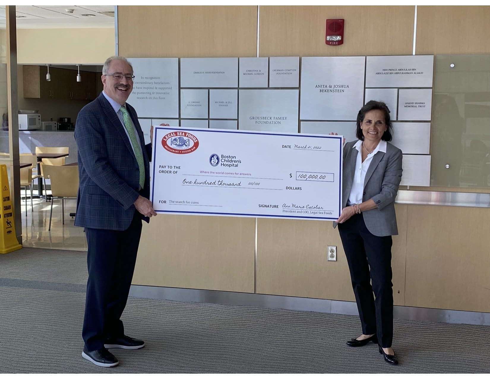 Two individuals stand in a lobby, each holding one end of a large novelty check made out to 