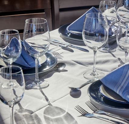 Elegant table settings with neatly arranged wine glasses, water glasses, silverware, and folded blue striped napkins on white tablecloths