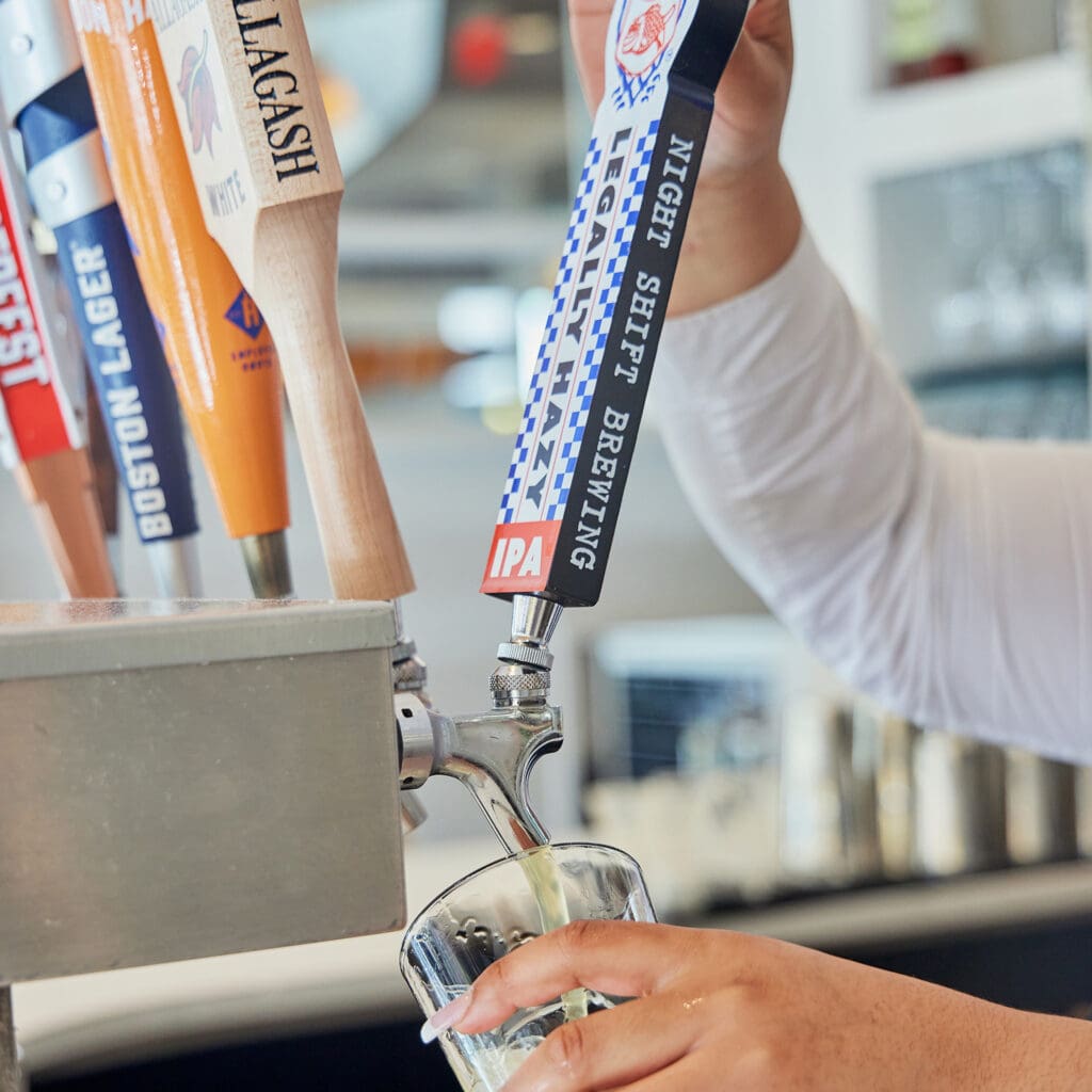 A person is seen pouring a draft beer from a tap labeled 